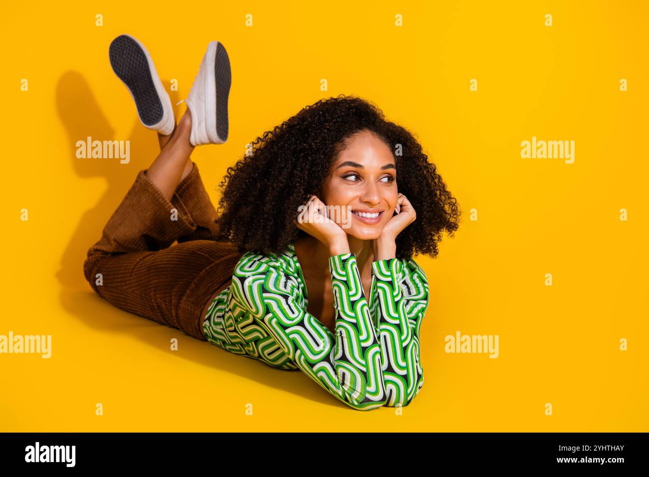 Charming young woman with curly hair in green top lying on yellow ...