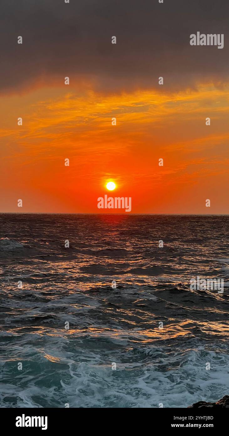 The sun rises over the ocean, casting a warm orange glow across the sky. The waves gently lap at the shore, creating a peaceful and serene atmospher - Smartphone Captured Stock Image