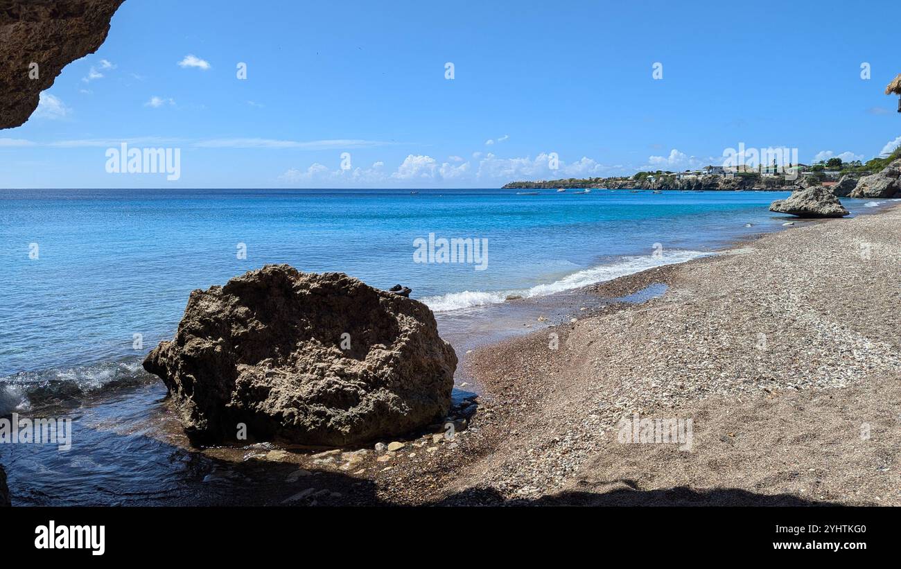 A large volcanic rock looks out to the ocean from a rocky beach on Curacao. August 2024. - Smartphone Captured Stock Image