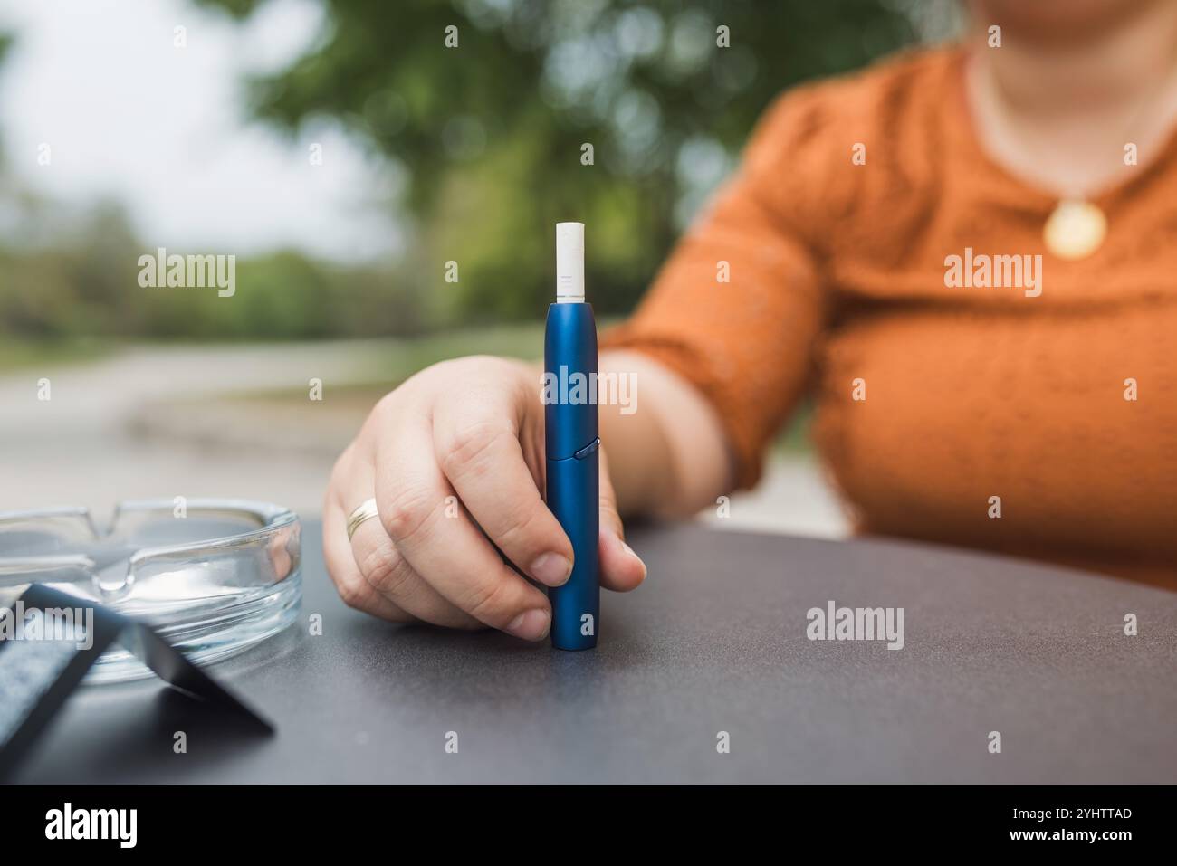 Smiling woman during a cigarette break, enjoying vaping outdoors. Concepts of heated tobacco products and modern lifestyles. Stock Photo