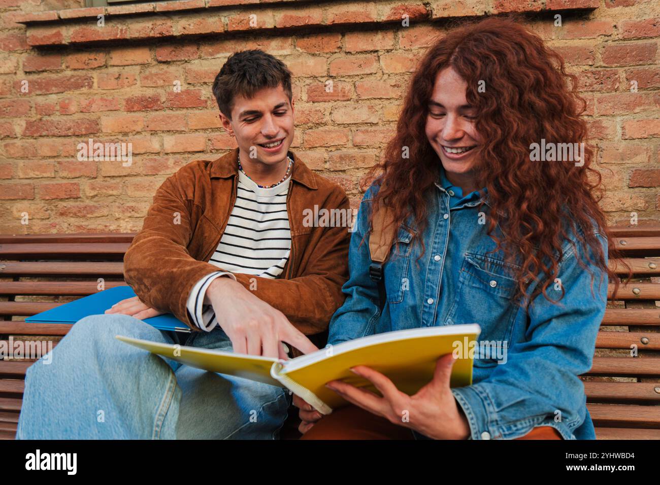 happy young university teenage students reading notebook and studying the lesson together while sitting on bench at university campus, high school or academy. Classmates doing the homeworks. High quality photo Stock Photo