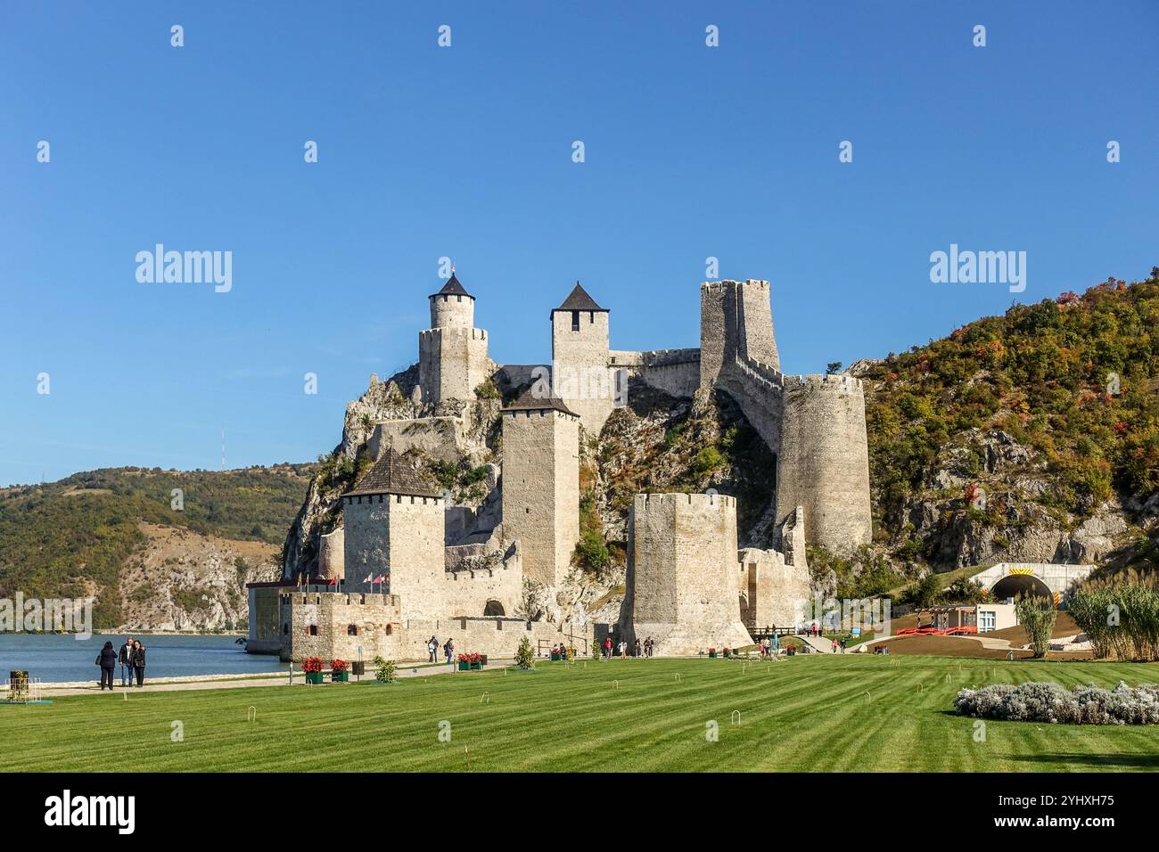 Golubac medieval fortress with multiple towers on a rocky hill beside a river under a clear blue sky, surrounded by the green landscapes of the Danube Stock Photo