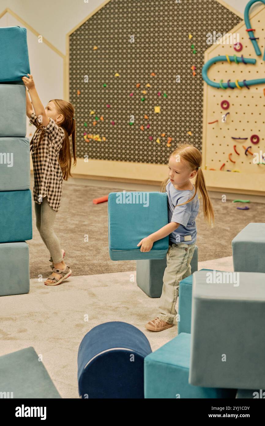 Cute blond little girl with two ponytails carrying big soft toy cube of ...