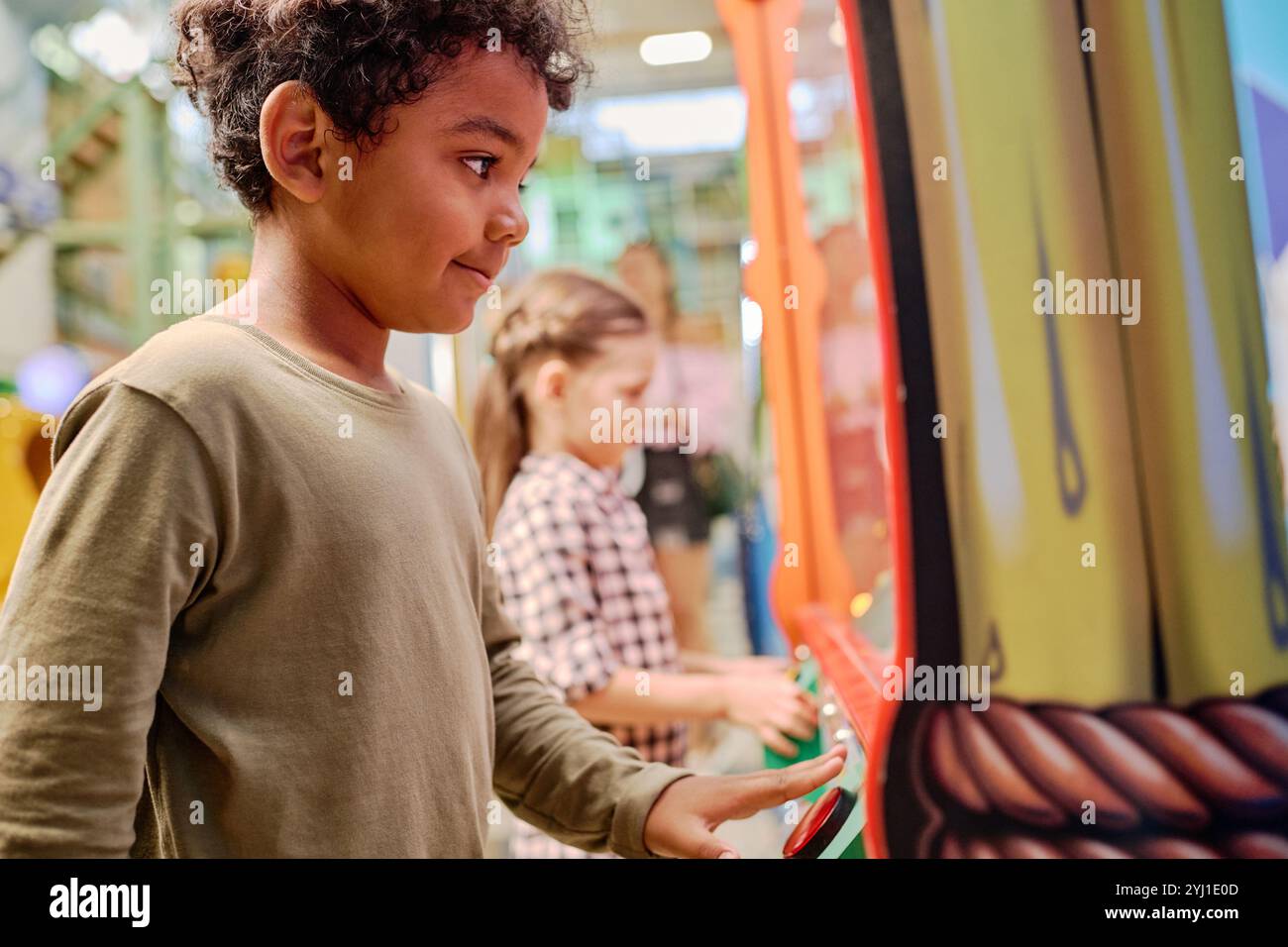 Cute African American boy pressing button and looking through glass of vending machine while trying to crane soft toy Stock Photo