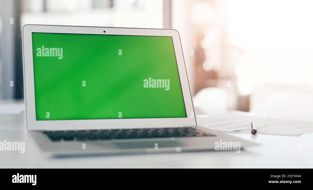 Green screen, table and laptop for mockup space, advertising promo or placeholder in office. Display, computer or monitor with chroma key for design Stock Photo