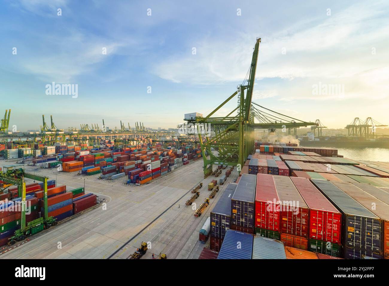 Sunrise over a busy container port with rows of colorful shipping containers, large cranes, and cargo handling equipment, Singapore Stock Photo