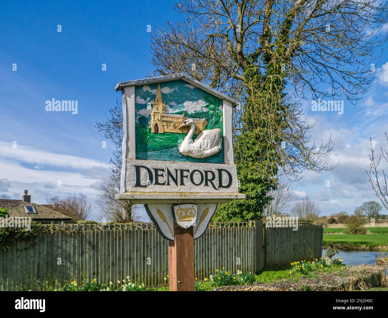 Colourful wooden village sign, Denford, Northamptonshire, UK; depicting the church of Holy Trinity and a white swan Stock Photo