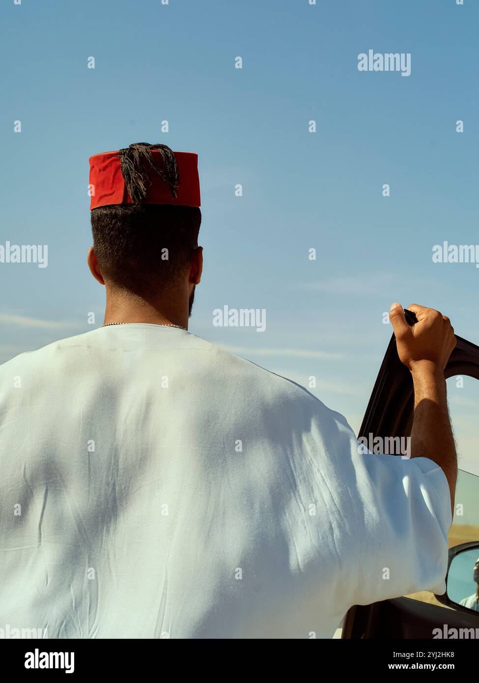 Man in traditional attire standing next to a car under a clear blue sky, Morocco Stock Photo
