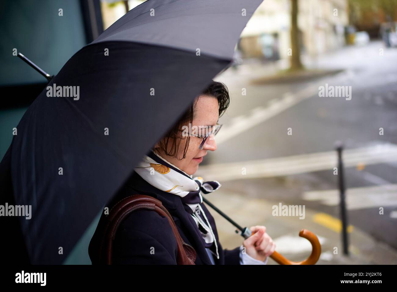 Woman with glasses holding an umbrella on a rainy day at a pedestrian ...
