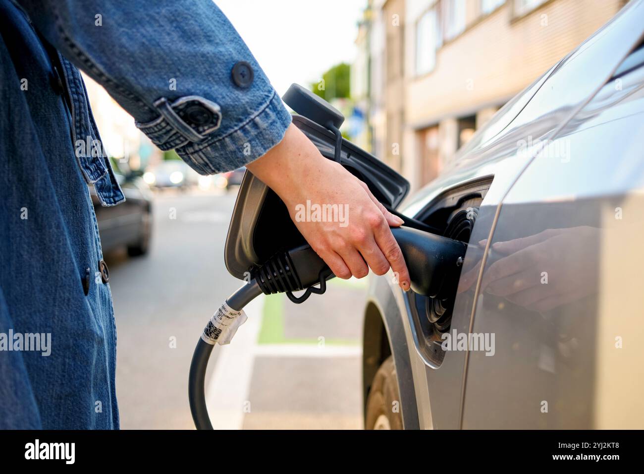 Close-up of a person's hand inserting a charging plug into an electric vehicle's charge port on a sunny day. Stock Photo