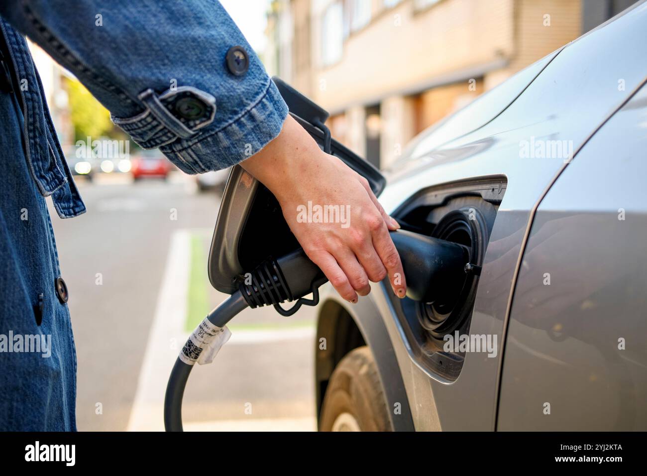 Close-up of a person's hand inserting a charging plug into an electric vehicle's charge port on a sunny day. Stock Photo