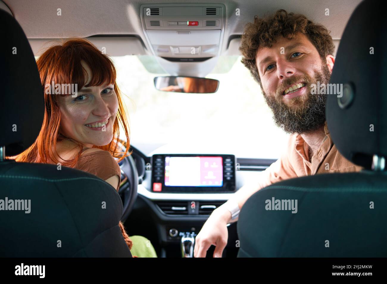 Smiling man and woman sitting in a car looking back at the camera and the woman in the passenger seat. Stock Photo