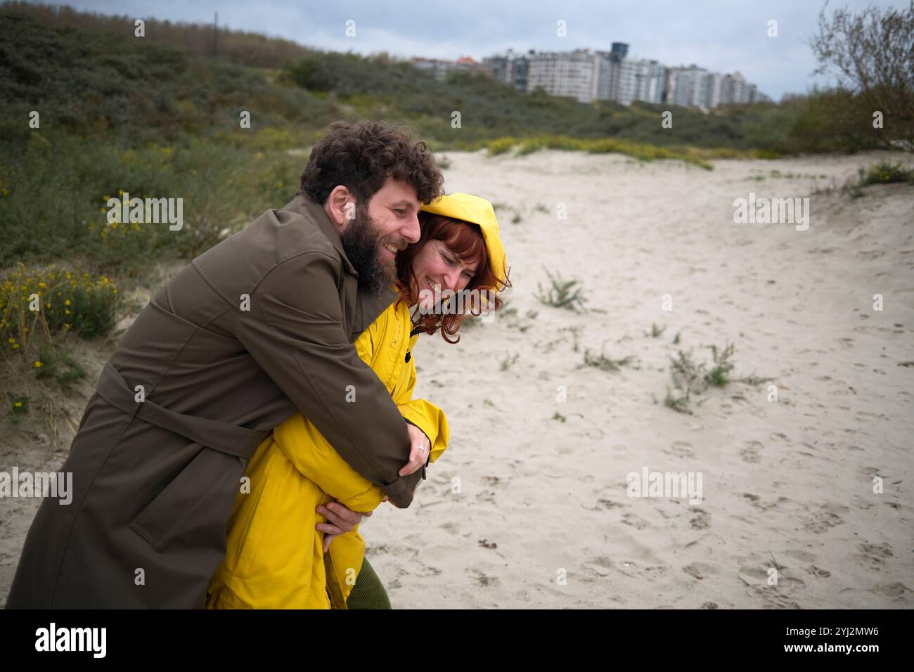 A couple in yellow raincoats embracing and smiling on a sandy beach ...