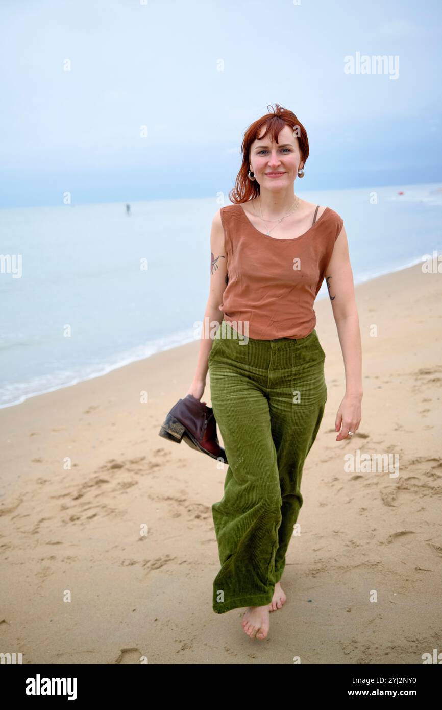 Woman walking barefoot on a sandy beach with the ocean in the ...