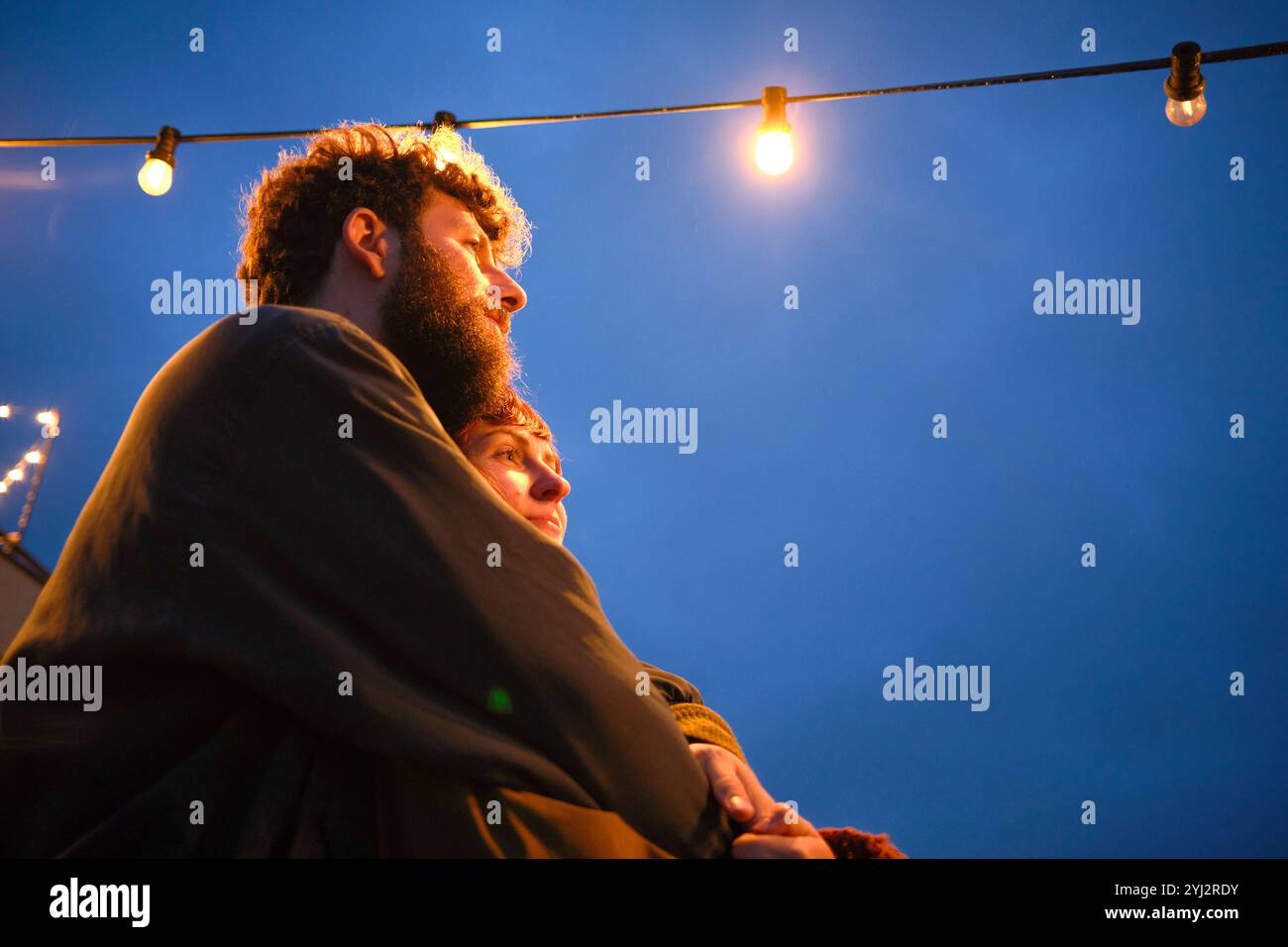 Couple embraces under a string of lights against a twilight sky, Belgium Stock Photo