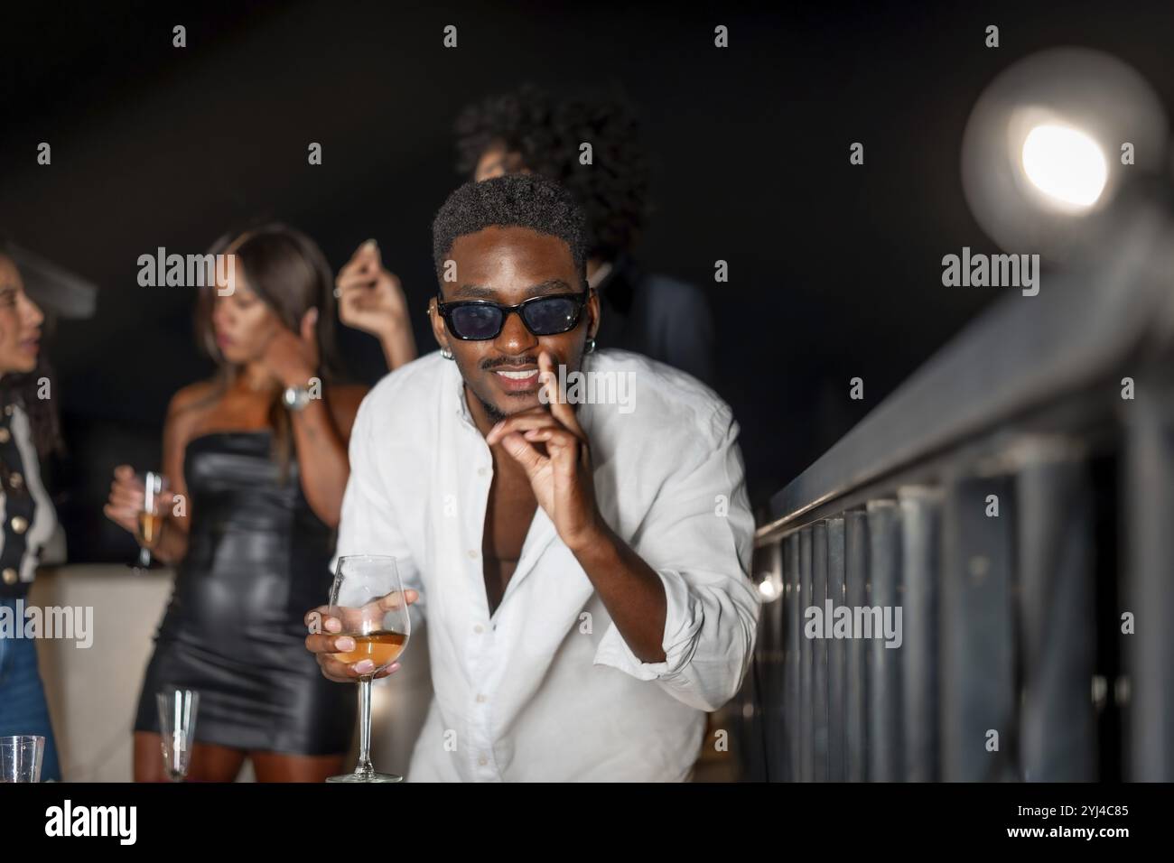 Latin cool man gesturing while dancing and drinking alcohol during roof party at night Stock Photo