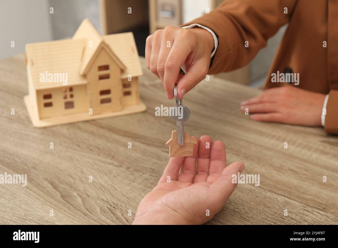 Real estate agent giving house key to new owner at wooden table ...
