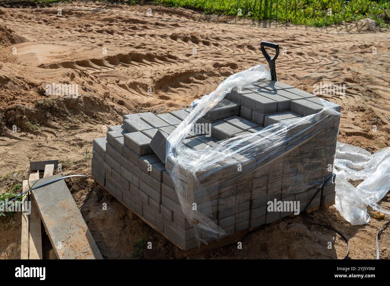 A stack of gray bricks is wrapped in plastic at a construction site ...