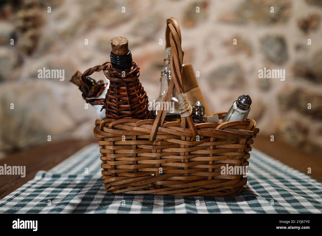 Wicker spice rack with vinegar, olive oil, salt and pepper on table. Stone wall background Stock Photo