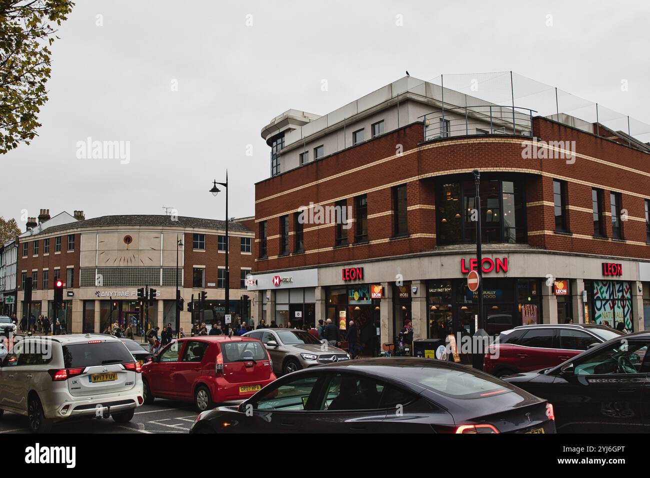 A street corner with a brick building featuring a large 'LEON' sign, a clock face on an adjacent building, and numerous cars and pedestrians. The sc Stock Photo