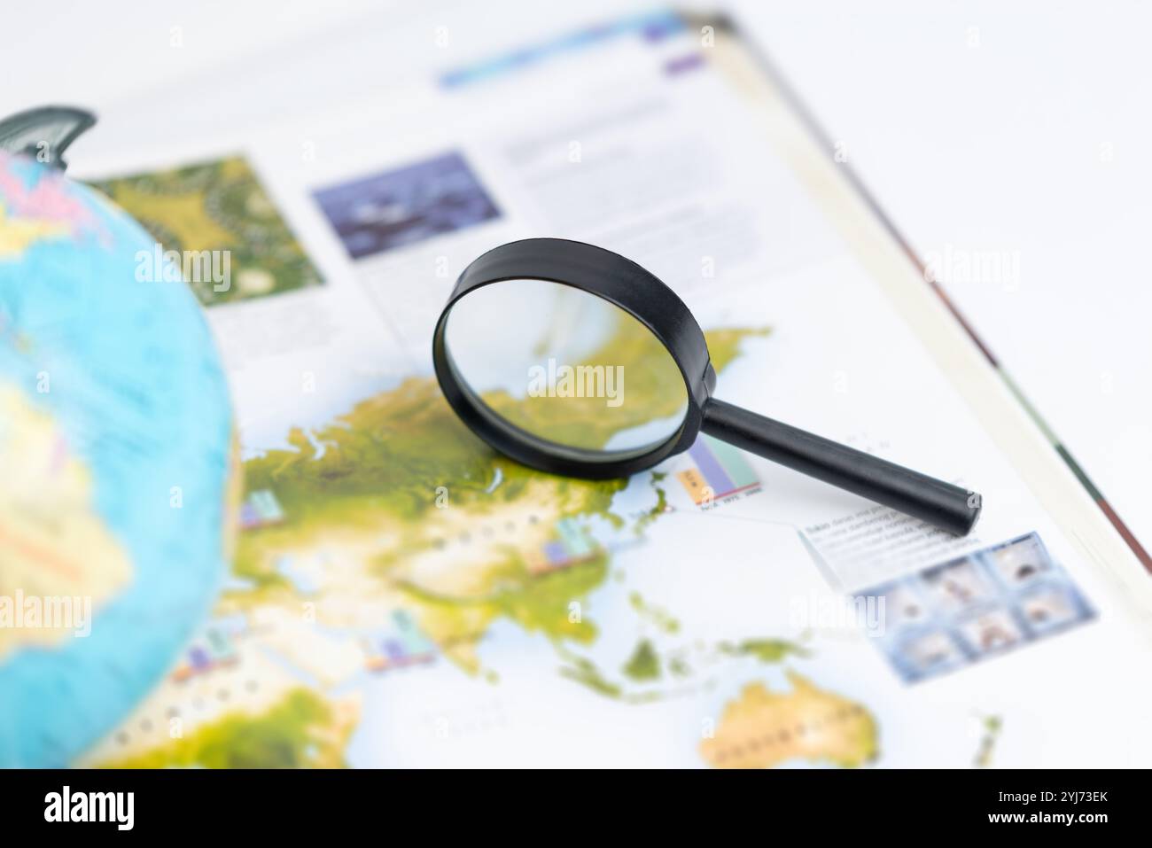 Magnifying glass on world atlas with globe nearby, symbolizing global exploration, travel planning, geographic research, and a deeper understanding of Stock Photo