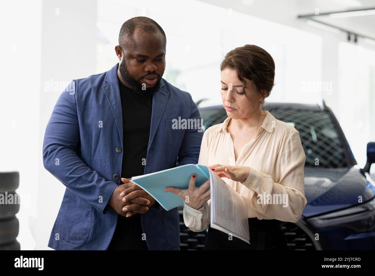 Customers in car dealership reading catalog, browsing through available