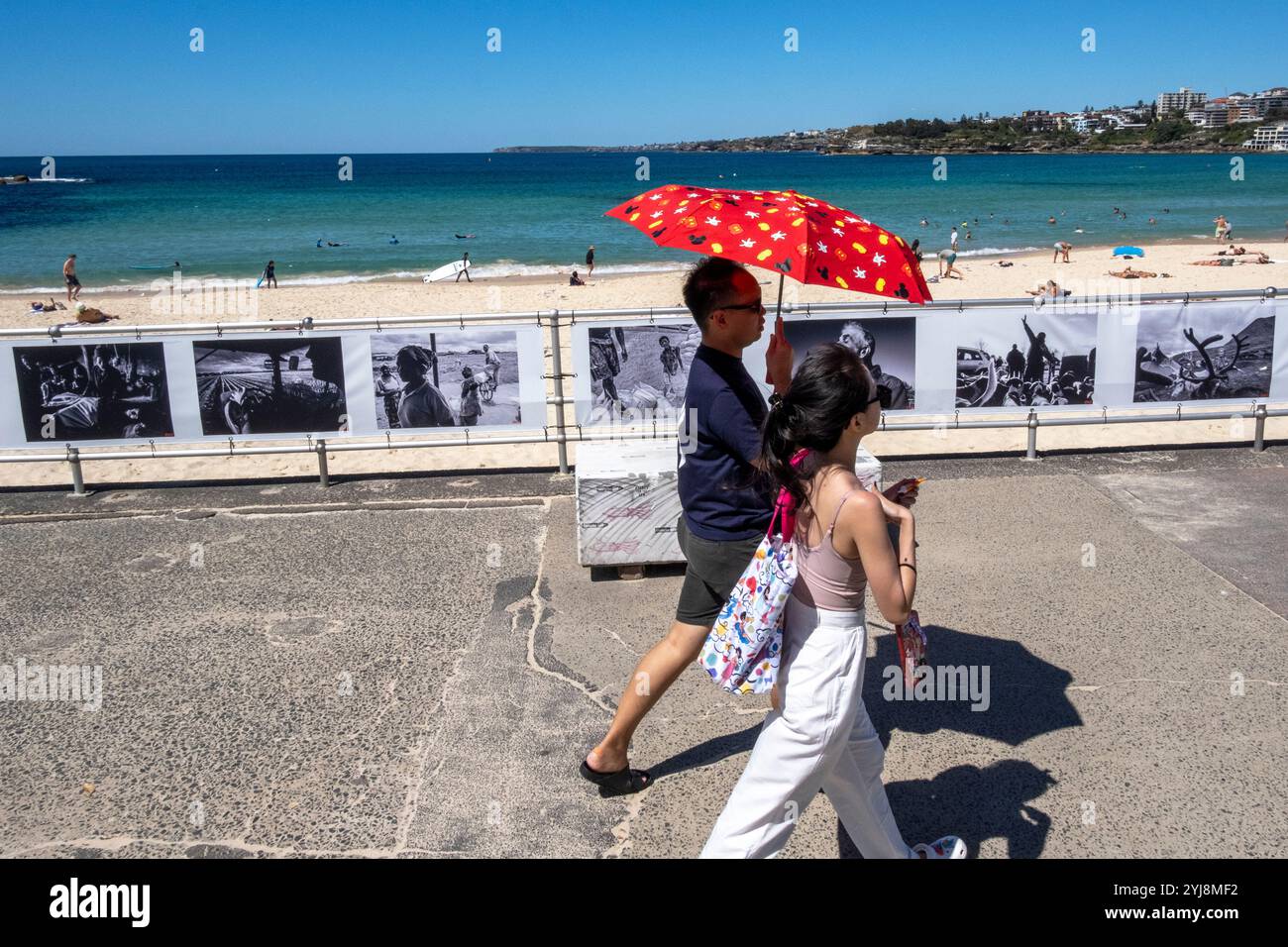 Pedestrians walk past a Head On Photo Festival exhibition hanging at Bondi beach, Sydney NSW, Australia Stock Photo