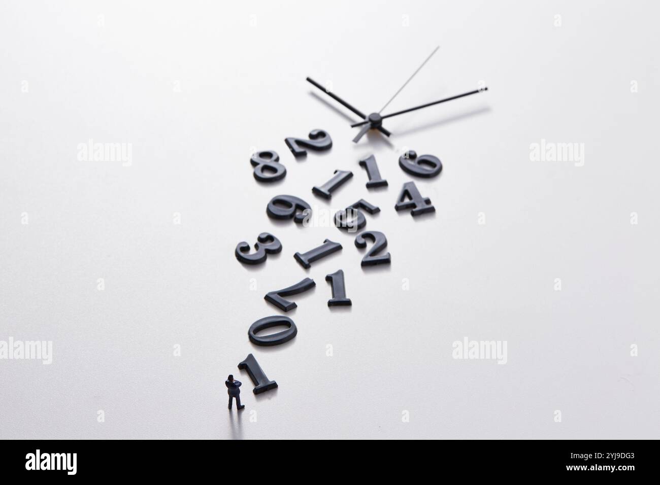Miniature doll standing in front of disjointed numbers and clock hands ...