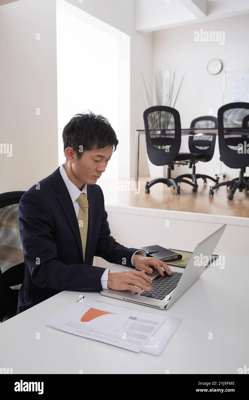 Man sitting on a chair in an office working on a computer Stock Photo ...