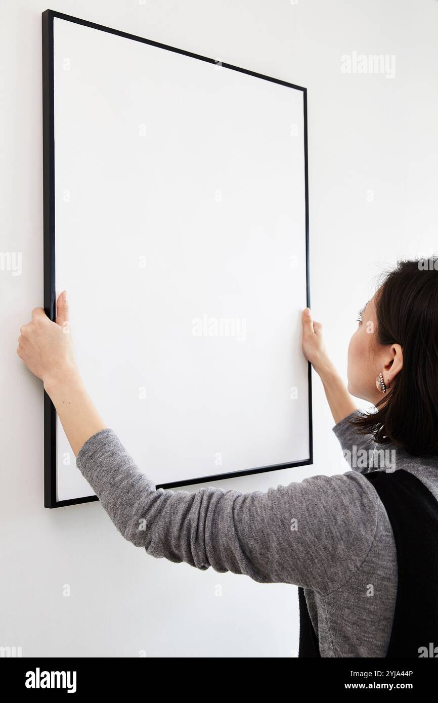 Woman hanging frame on wall Stock Photo