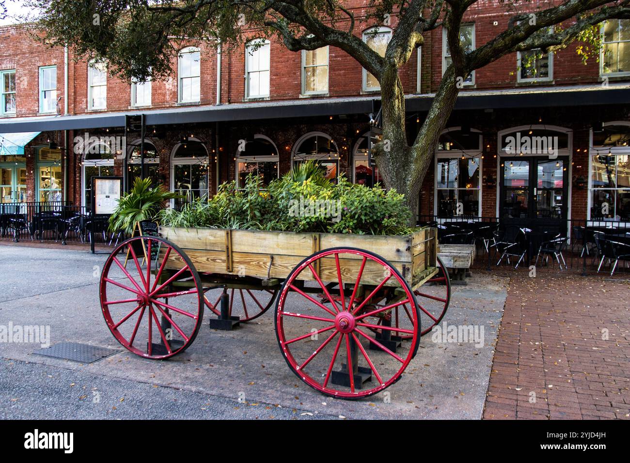 Savannah, Georgia, USA - 20 February 2024: A colorful wagon overflowing with plants sits near a lively restaurant area, enhancing the local charm. Stock Photo