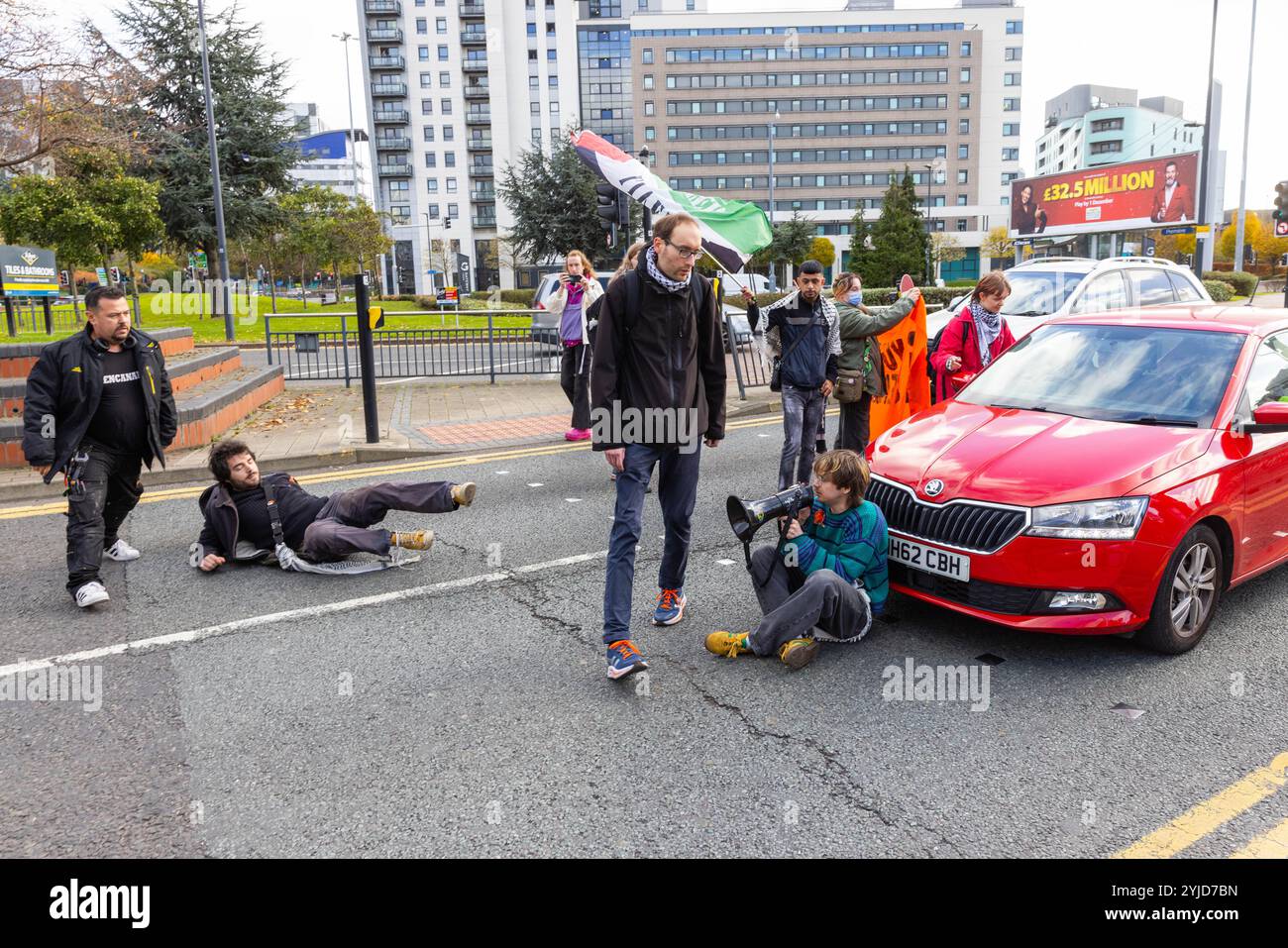 Leeds, UK. 14 NOV, 2024. Road blocked as protestors from action group Youth Demand stepped out in the road for the 3rd time this week, in a nationally co-ordinated action seeing small swarms block traffic for up-to 15 minutes aiming to highlight the ongoing situation in Palestine. During todays action a number of irate drivers physically moved and grabbed at the protestors, the activists did not fight back but did not leave the road, police were called but did not attend,. Credit Milo Chandler/Alamy Live News Stock Photo