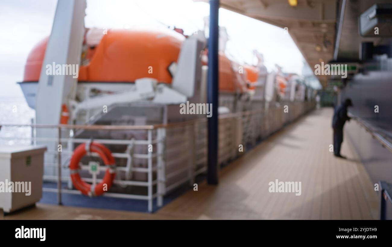 Blurred man stands on a cruise deck with lifeboats, showcasing an out-of-focus scene with bokeh lighting and a defocused ocean background for travel i Stock Photo