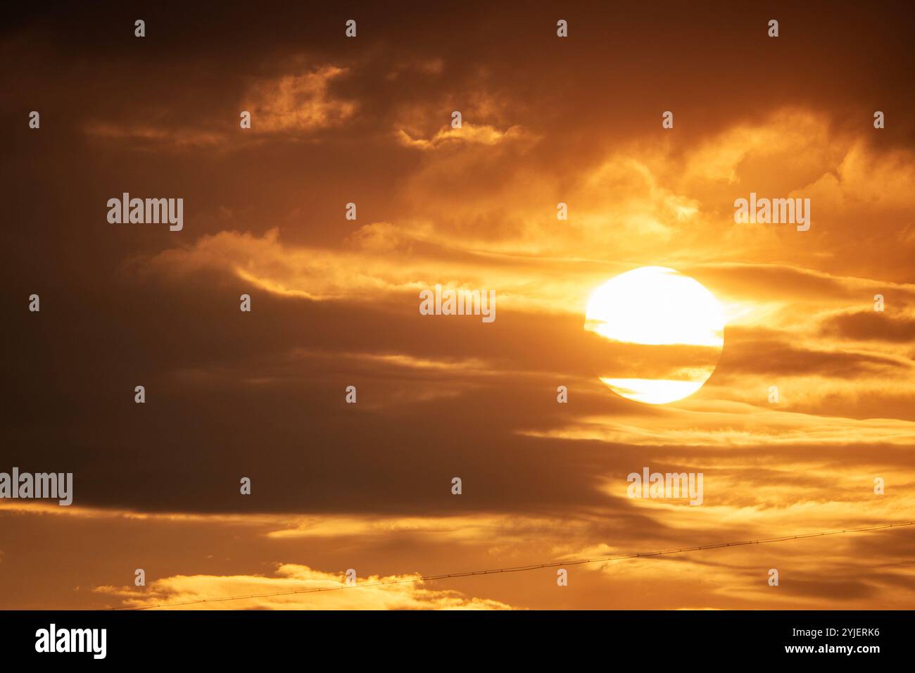 A dramatic view of the sun setting behind layers of clouds, casting a warm, golden light over the sky Stock Photo