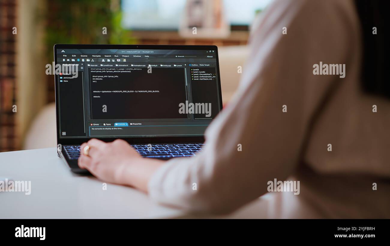 Asian female programmer works on coding software in a home office setup, typing code on a laptop. IT expert uses digital tools for multitasking, software development and app development. Camera B. Stock Photo