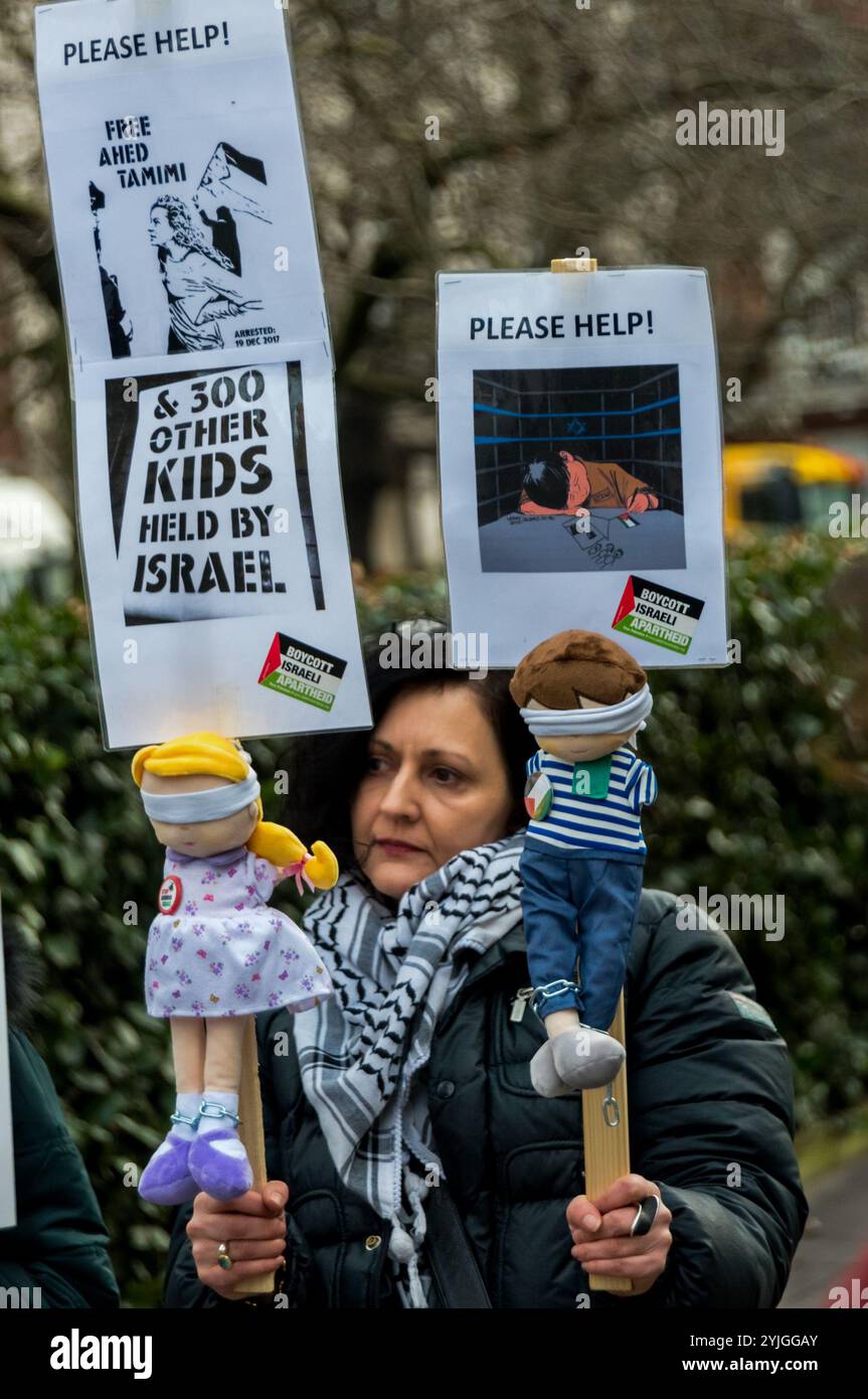 London, UK. January 13th 2018. A protester at the US Embassy in Grosvenor Square holds up placards with blindfolded male and female dolls representing child prisoners calling for help. The protest called for the release of all child prisoners held in Israeli jails, including Ahed Tamimi, held for slapping an Israeli soldier who came into her family's garden shortly after she had learnt that a relative had been shot by Israeli forces. She is one of the thousands of Palestinian children have been detained by Israel since 2000 in a systematic policy which the UN has said includes abuse and ill-tr Stock Photo