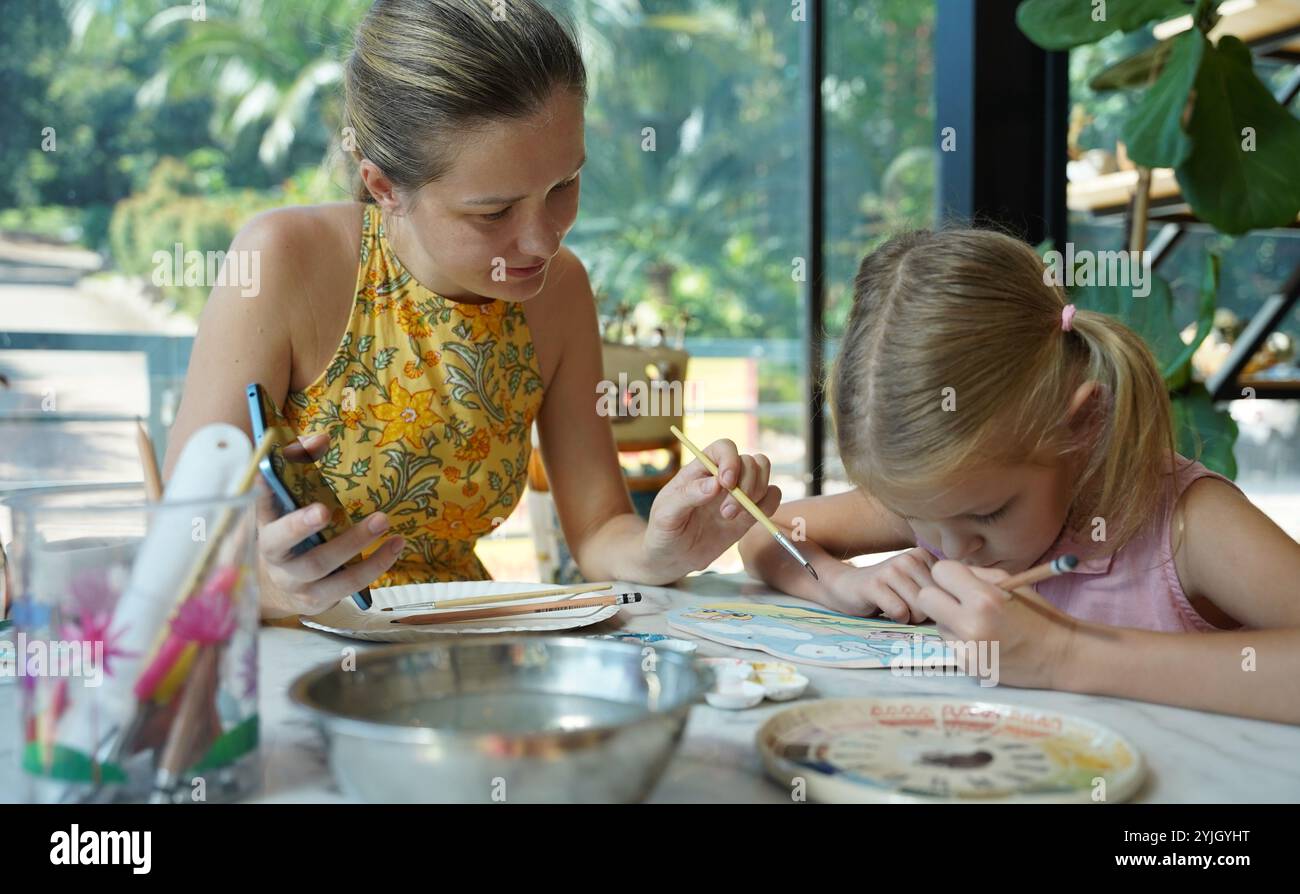 A young mother and her daughter enjoy a creative art session at home ...