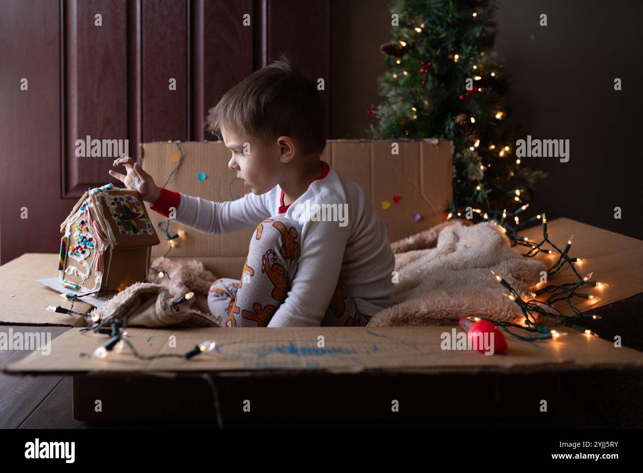 Young boy sitting in cardboard box playing with gingerbread house Stock Photo