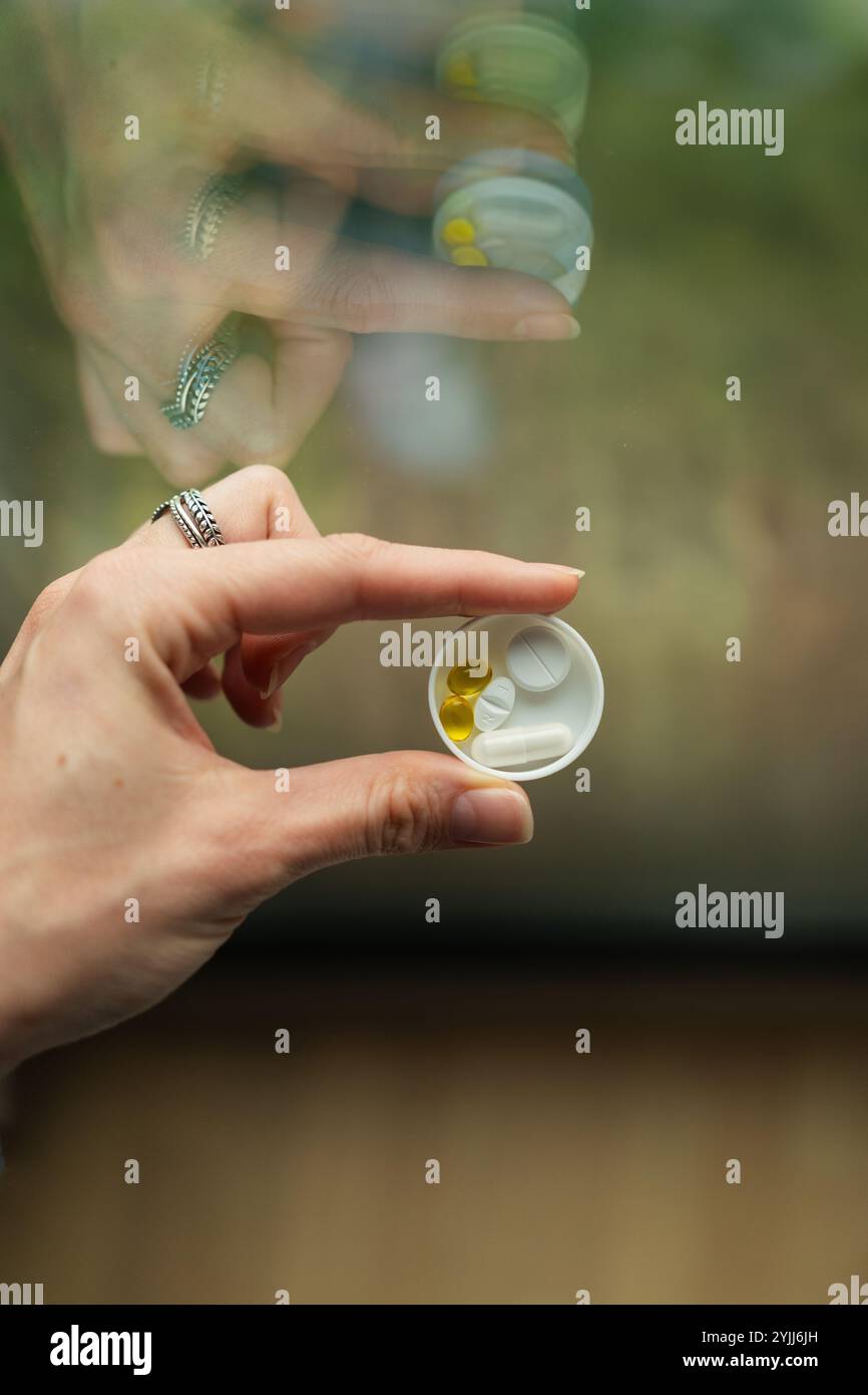 Close-up of woman's hand holding a dose of pills in front of window Stock Photo