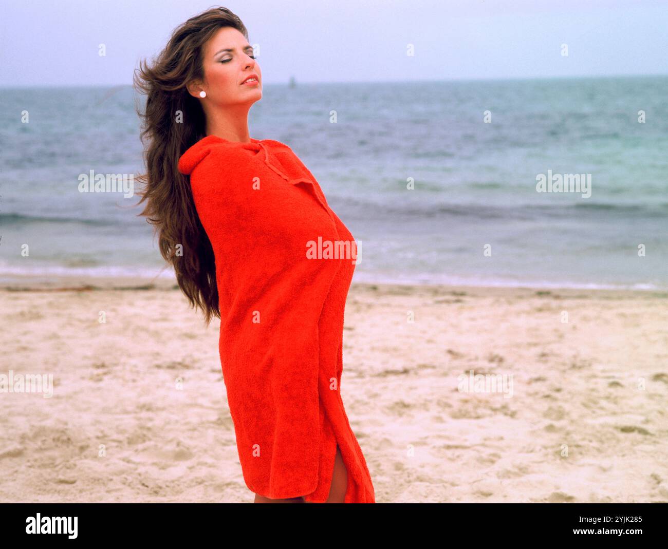 Young woman in red towel standing on the beach. Stock Photo