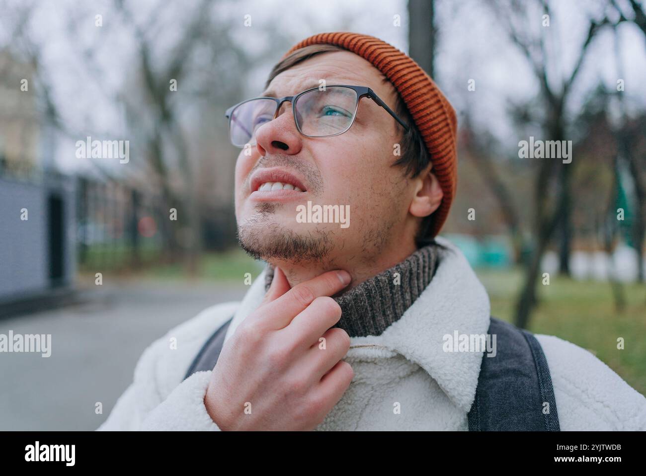 Young man wearing glasses and winter clothes touching his painful neck ...