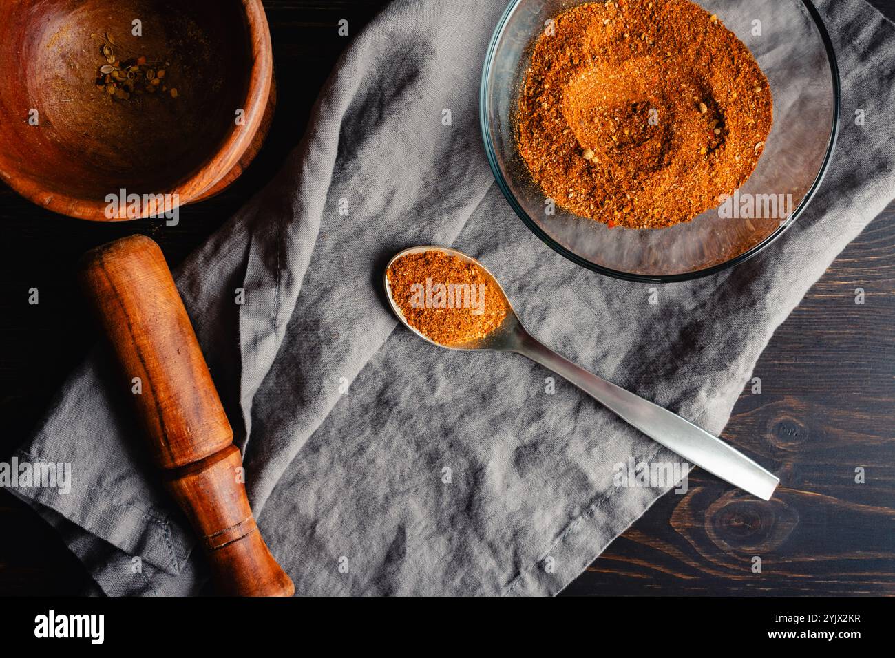 Spoonful of Homemade Berbere Spice Blend: Mixture of ground herbs and spices in a metal spoon next to a glass bowl and wooden mortar and pestle Stock Photo