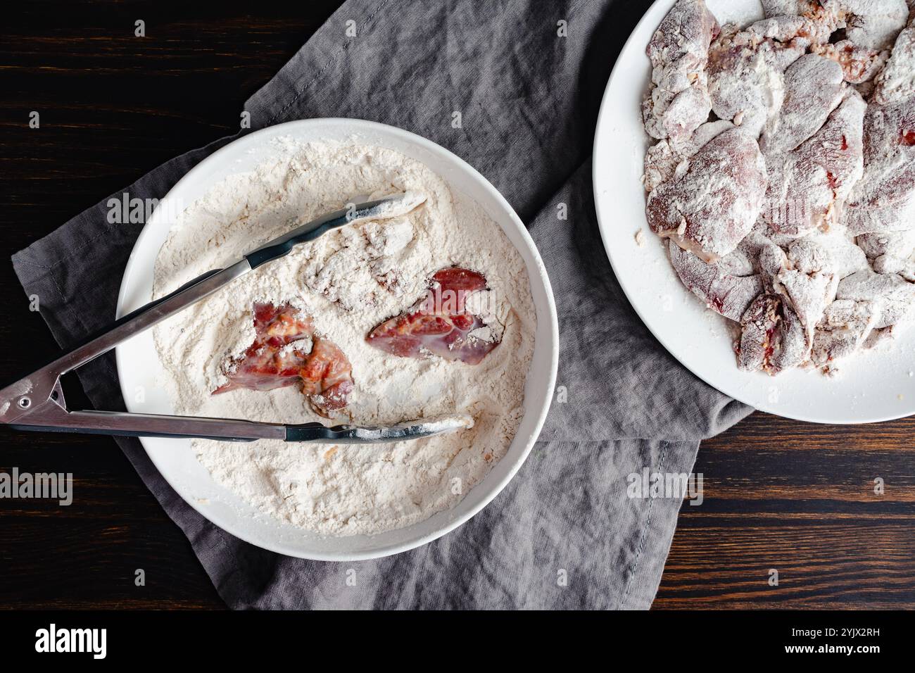 Breaded Chicken Livers Soaked in Milk: Tongs used to dredge raw chicken livers in a bowl of spiced and seasoned flour Stock Photo