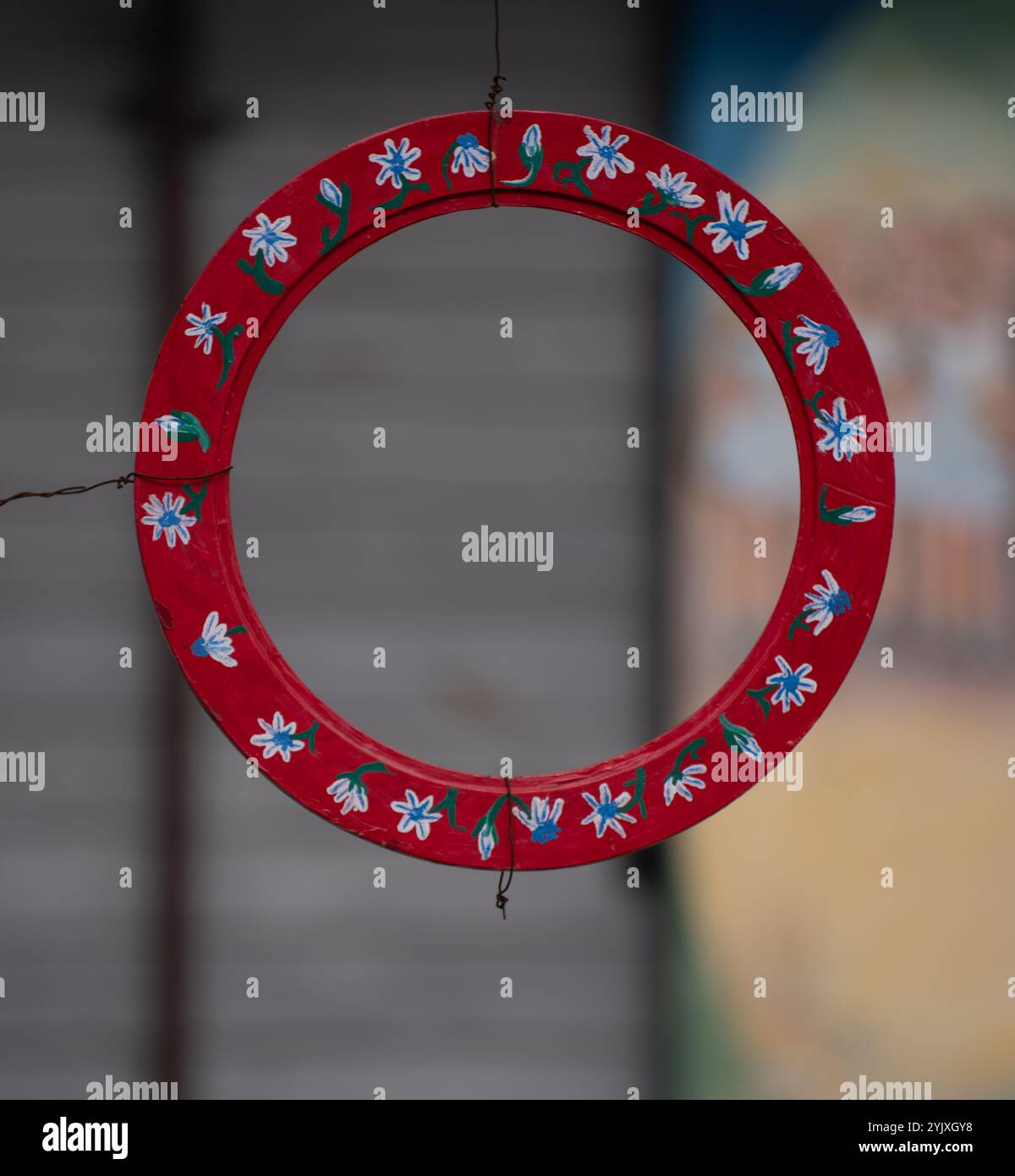 Hand painted red with white and blue  flowers round circular empty wooden frame hanging by a wire with blurred pastel colored background or backdrop h Stock Photo