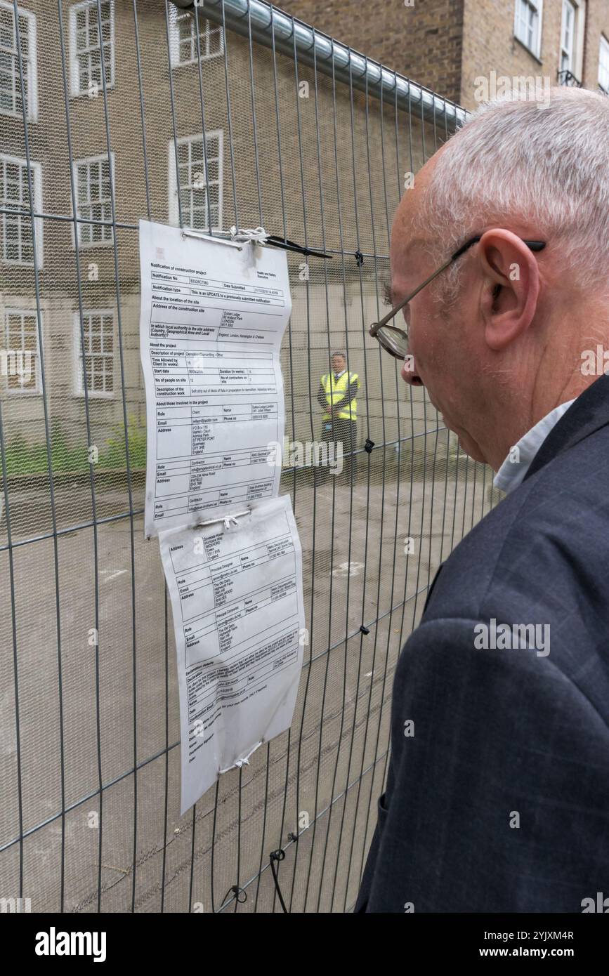 London, UK. 10th August 2017. Ian Bone of Class Was and the Peoples Republic Of North Kensington, an organisation supporting the former residents of Grenfell Tower, reads the notice on the fence  of Duke's Lodge, a large block of flats in Holland Park. The Campaigners demand thatKensington & Chelsea Council to compulsory purchase the empty block and refurbish its 27 flats as housing for families displaced by the Grenfell fire, around a 15 minute walk away. TIan Bone of Class War, who lived in Grenfell for three years in the 1980s, spoke at hte protest. The vacant block is owned by the Candy br Stock Photo