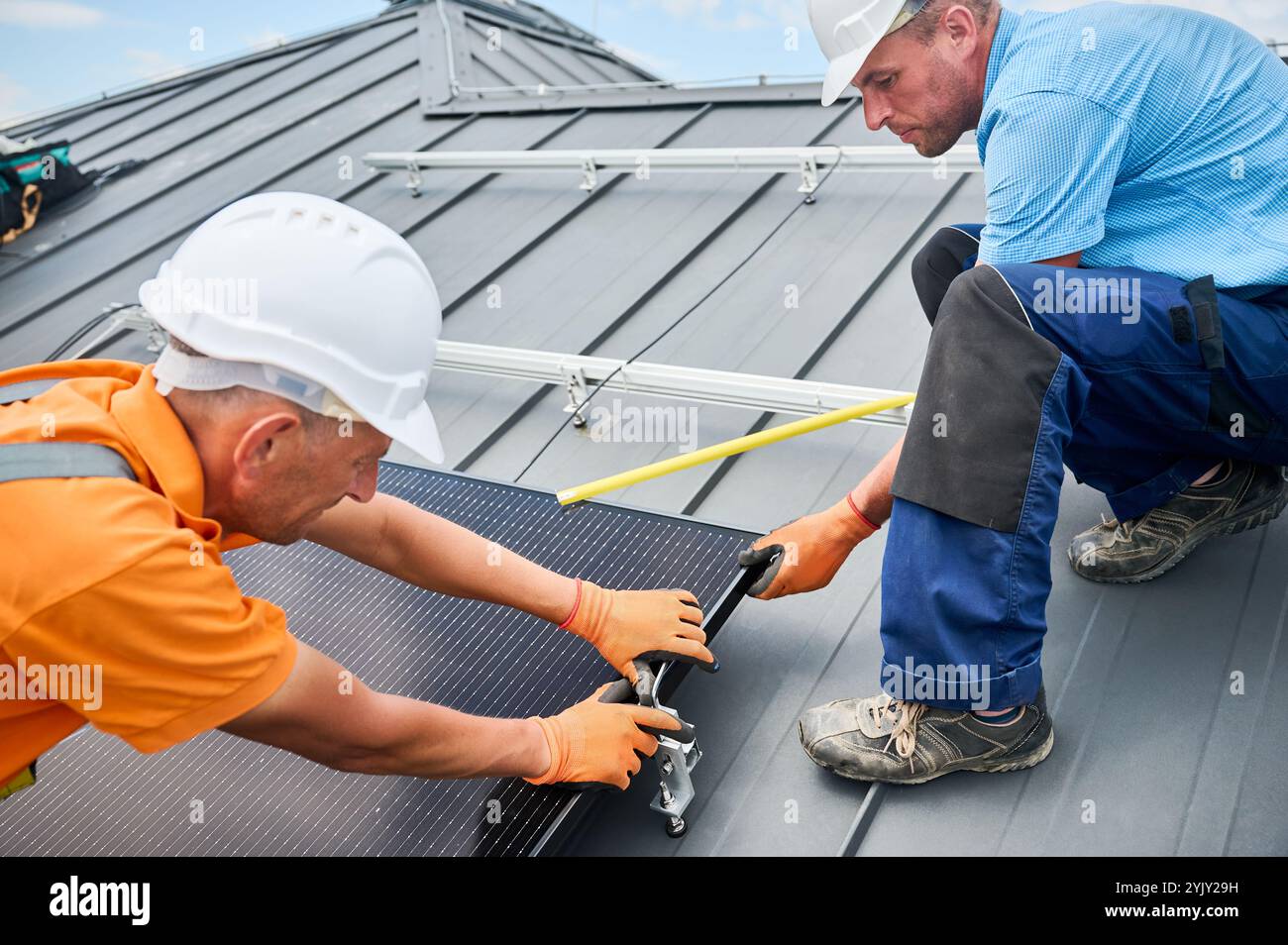 Workers building photovoltaic solar panel system on rooftop of house ...