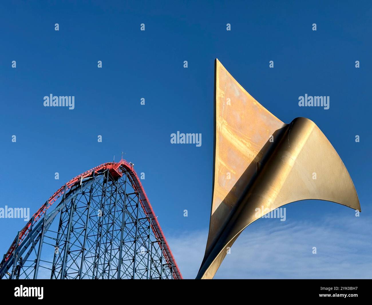 Abstract fin (Whale's Tail) on bench on Blackpool South promenade with the Big One rollercoaster ride in background against a blue sky. Blackpool, UK - Smartphone Captured Stock Image