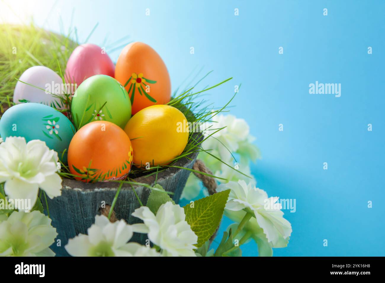 Happy Easter. Colorful Easter eggs and white flower on blue background.Copy space Stock Photo