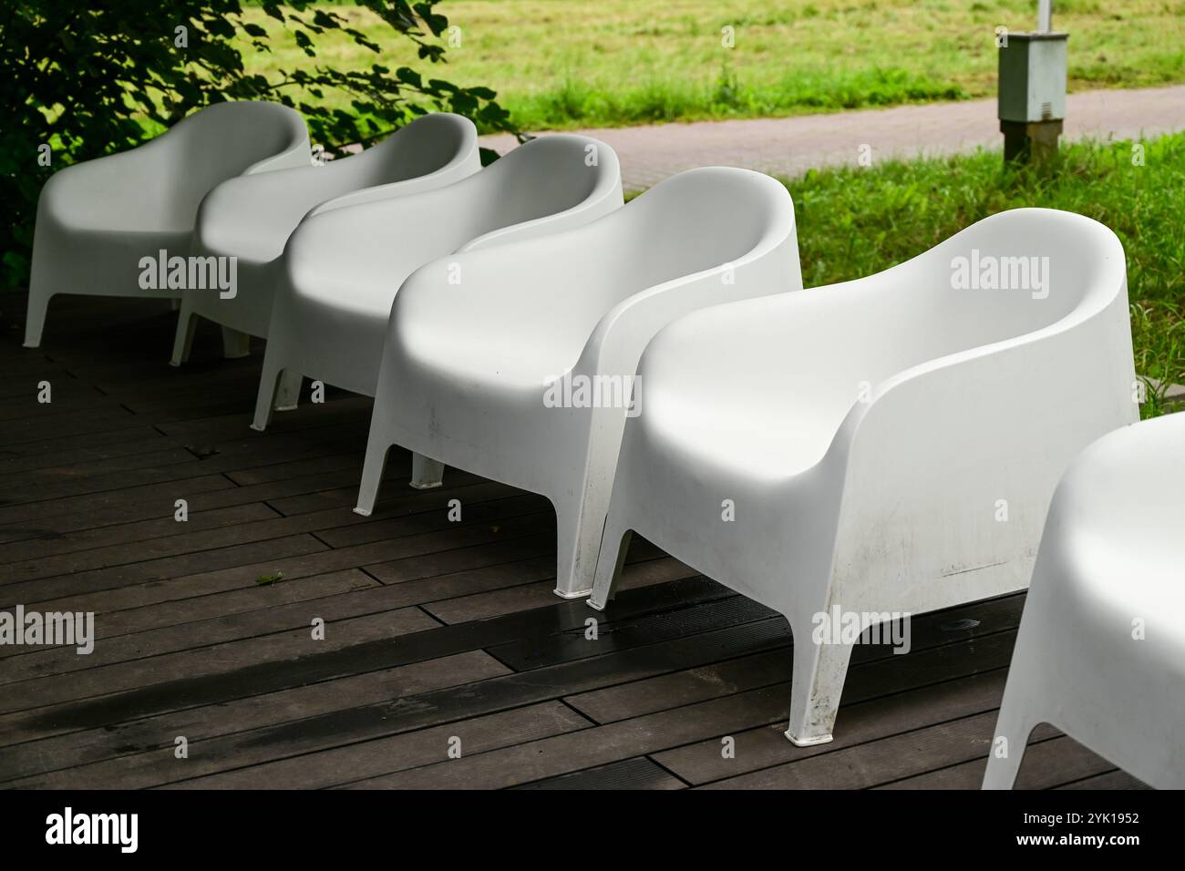 six white modern plastic garden chairs in a road on a wooden terrace of a restaurant Stock Photo