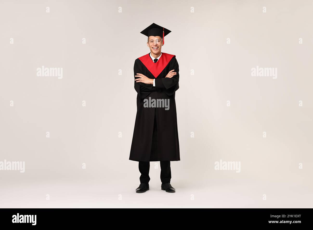 Happy student with crossed arms after graduation on light grey ...